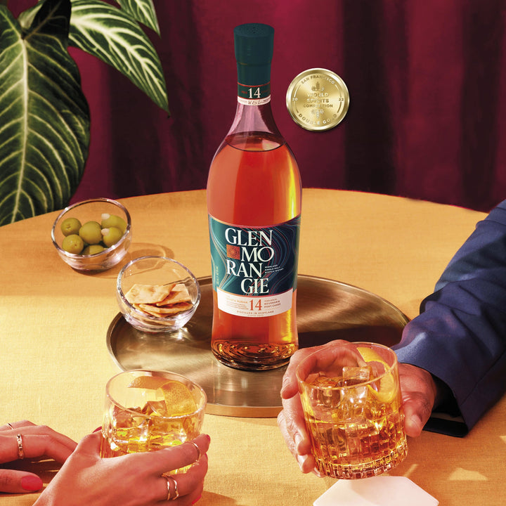 Glenmorangie whisky bottle with two glasses on a table, surrounded by decorative elements.